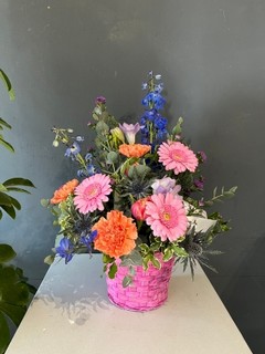 Hot pink wicker basket arranged with finest blooms to include roses, delphiniums, daisies, carnations, scented freesias and double tulips with eucalyptus By florist in Croydon, Surrey, UK